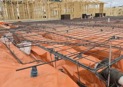Construction site with rebar framework and plastic sheeting for a concrete foundation near wooden framing.