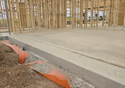 Freshly poured concrete foundation with wooden house framing in the background.