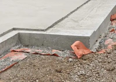 Close-up of a concrete foundation edge with reinforcement and orange safety barrier.